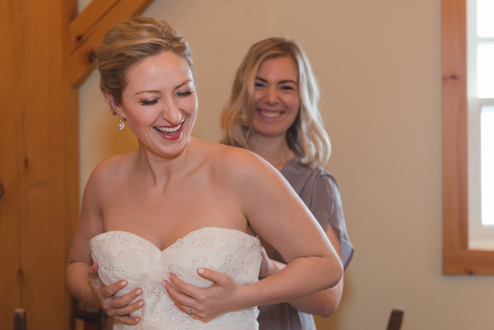 Bridesmaid helping bride put on her wedding dress