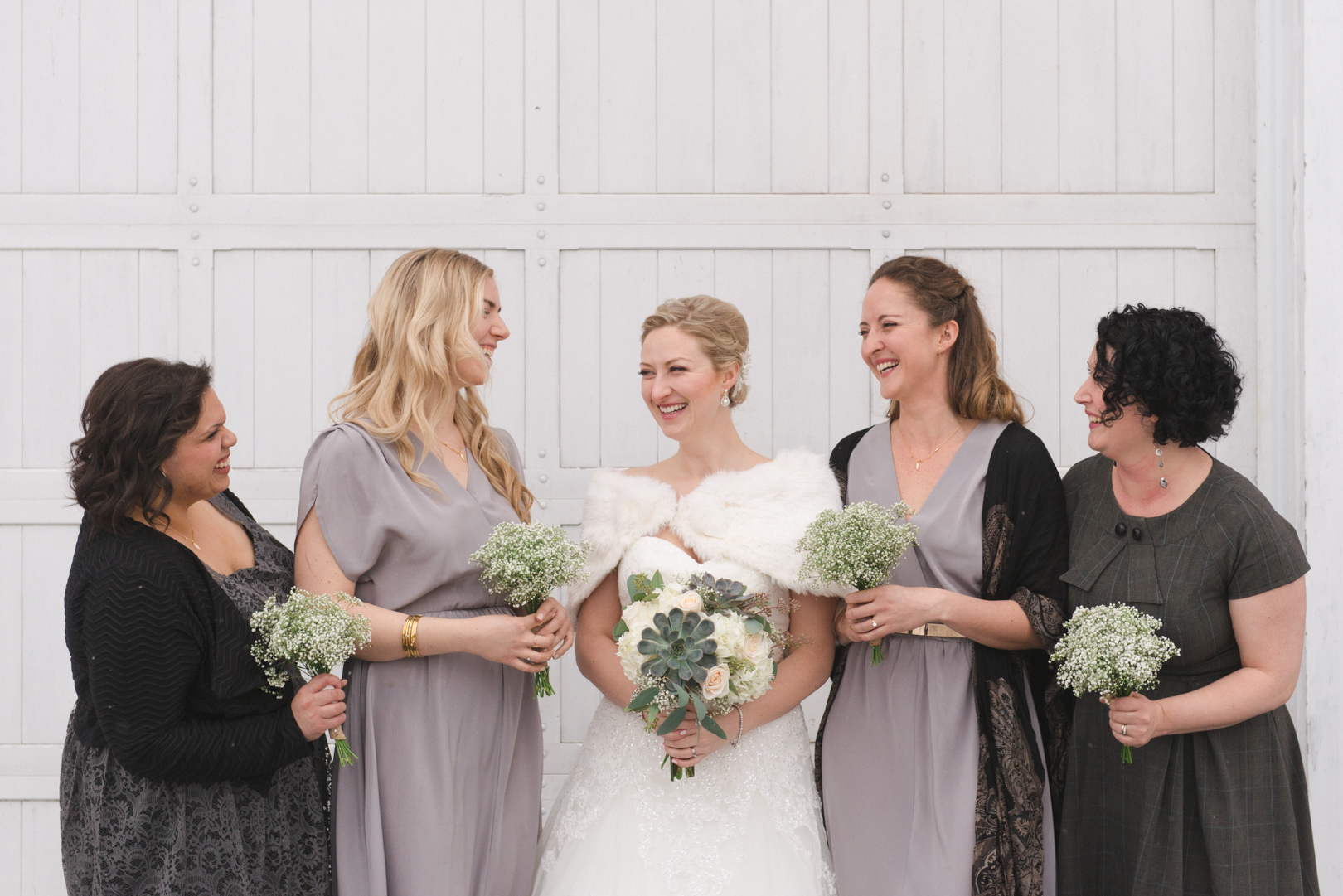 Bride and bridesmaids laughing in front of white door at Temples Sugar Bush