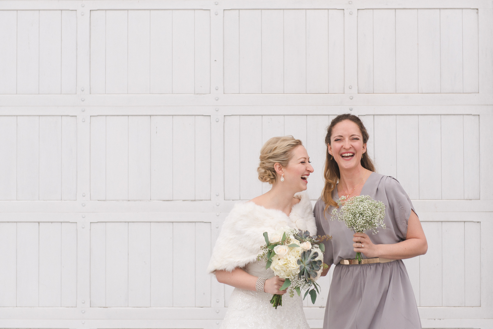 Bride and bridesmaid laughing in front of white door at Temples Sugar Bush