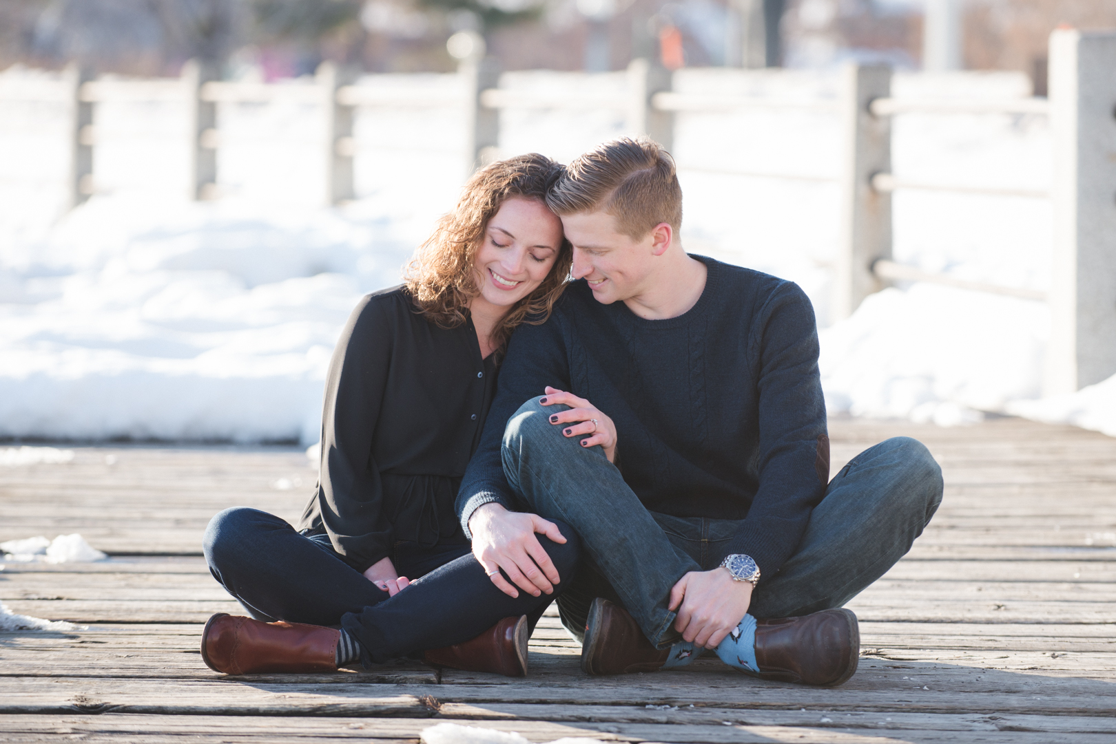 Couple sitting on wooden boardwalk on snow covered path during engagement photo session