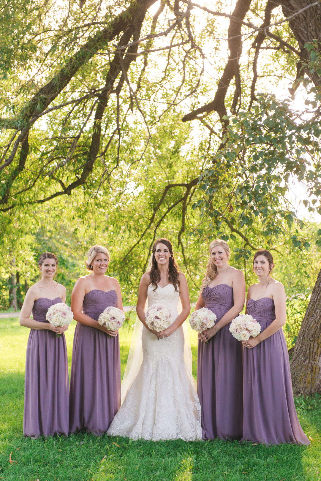 bride and bridesmaids standing underneath a tree