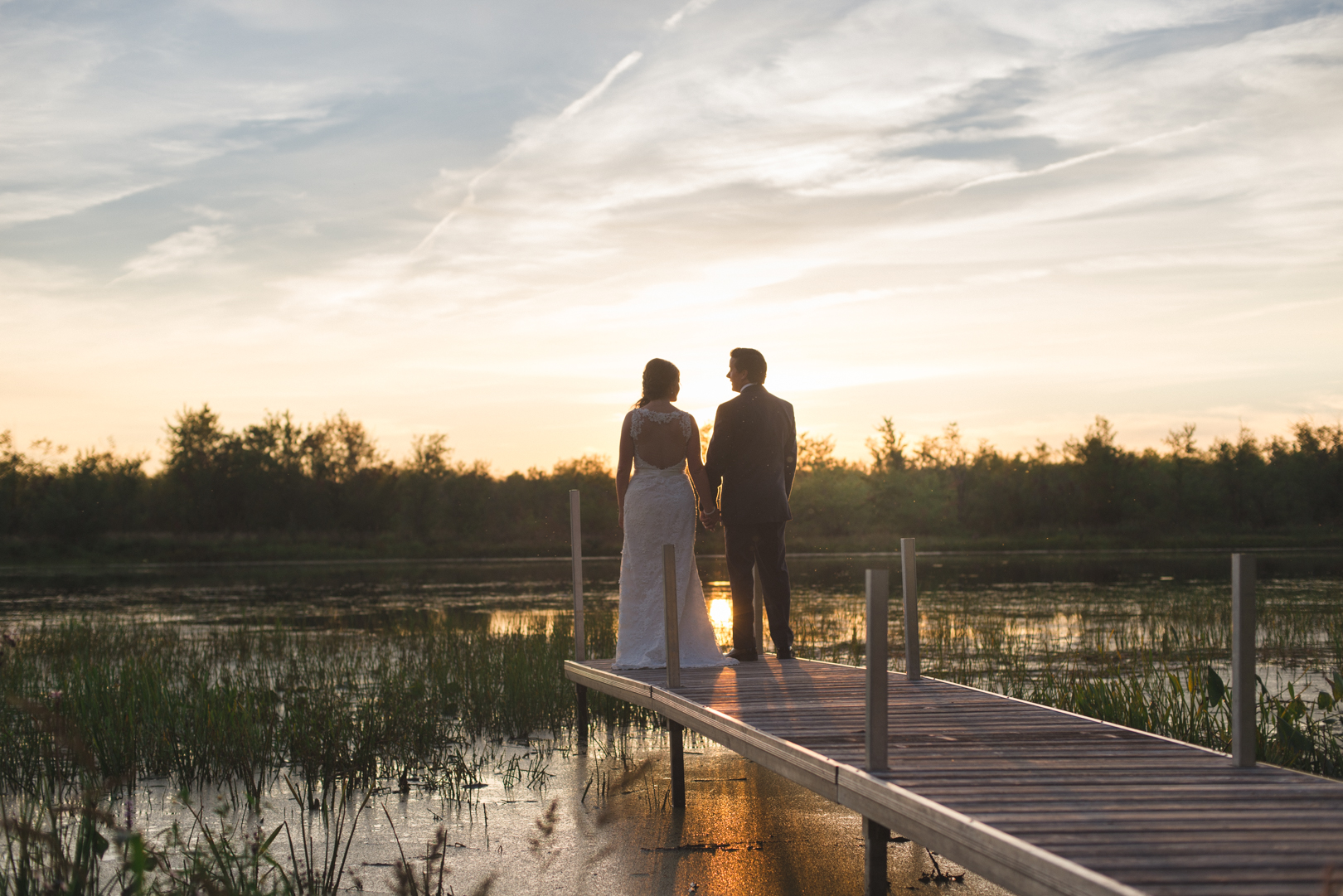 bride and groom at the end of a dock at sunset