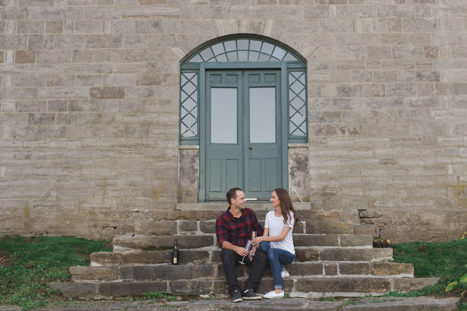 engaged couple having a glass of champagne on the steps at pinhey's point historical site