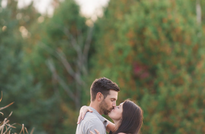 couple kissing with fall trees in the background