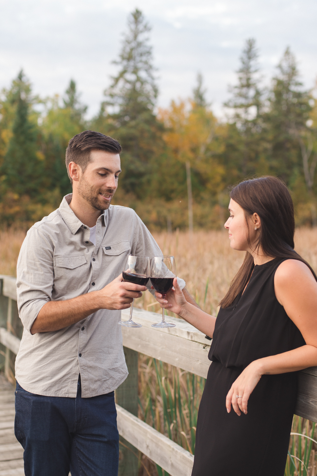 engaged couple enjoying a glass of wine together in the woods