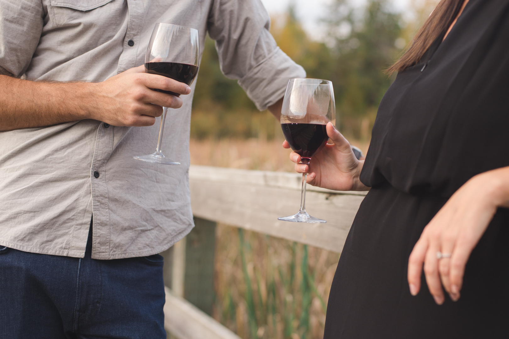 engaged couple holding a glass of red wine in the wilderness