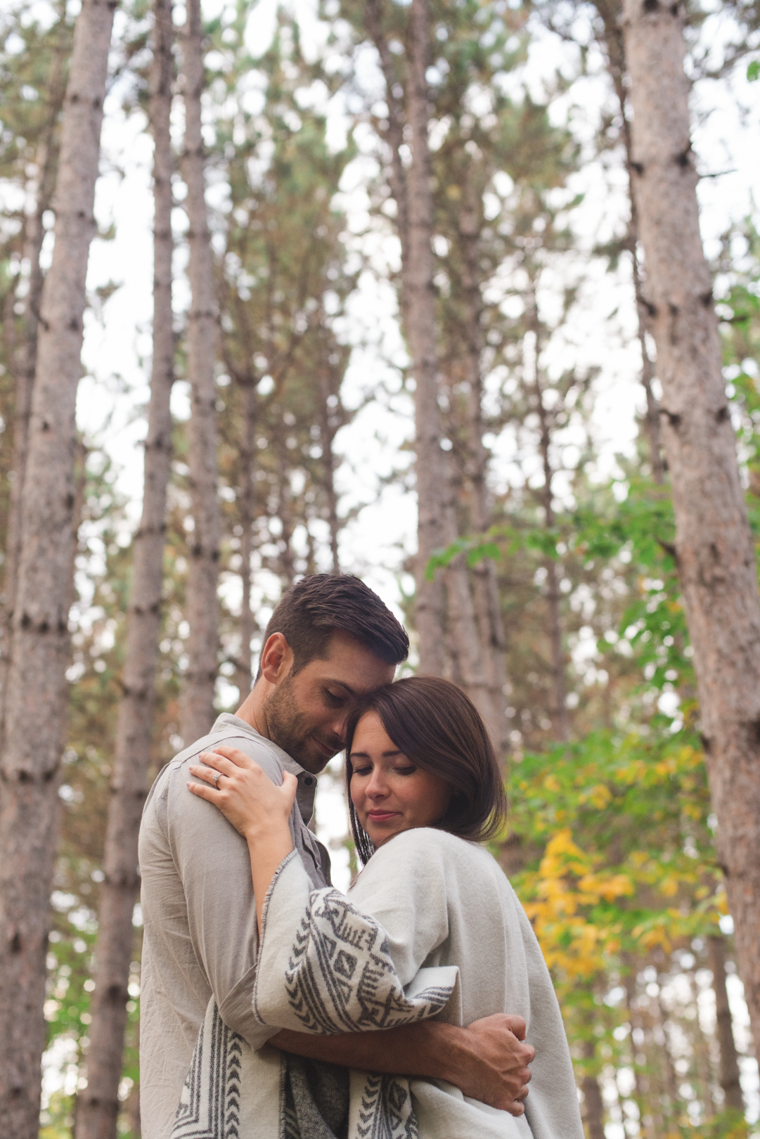 engaged couple cuddled among the tall trees in the forrest