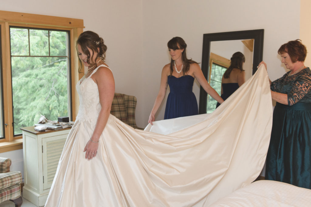 maid of honor and mother of the bride helping bride into her dress