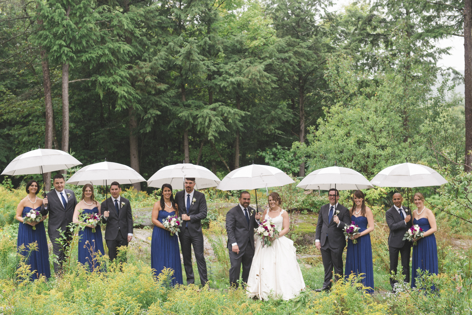 wedding party standing in the rain with umbrellas at le belvedere