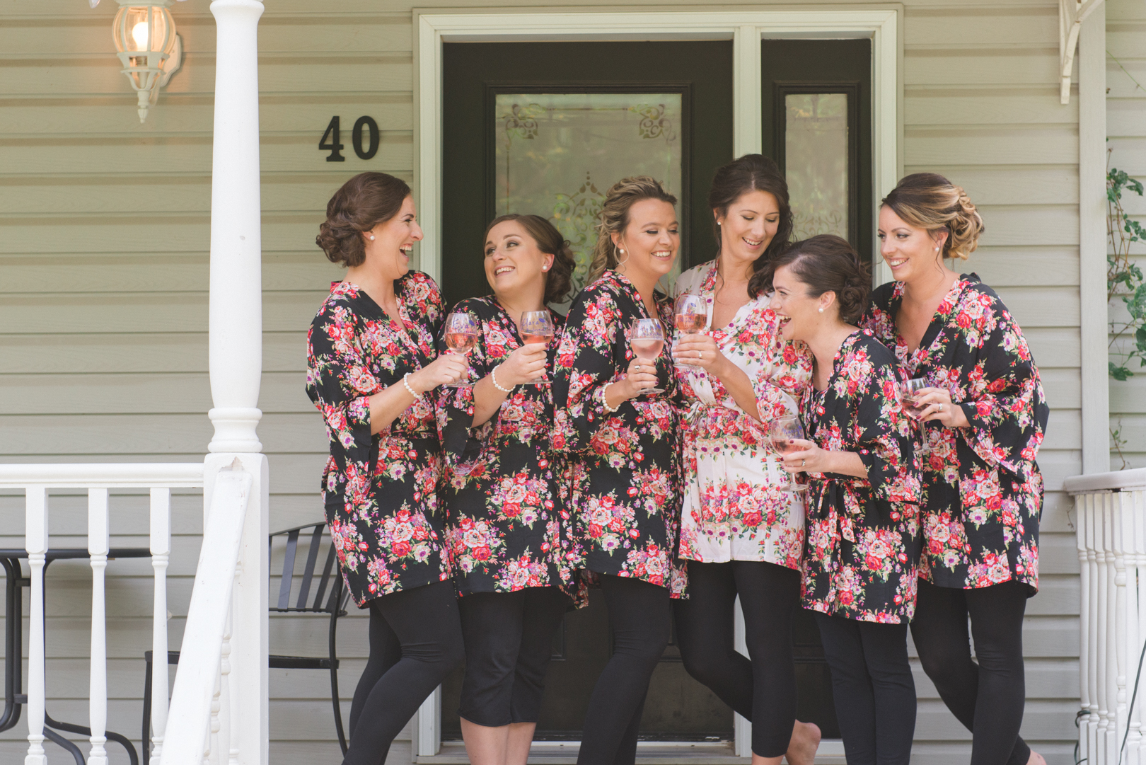 bride and bridesmaids in floral robes standing on the front porch with wine