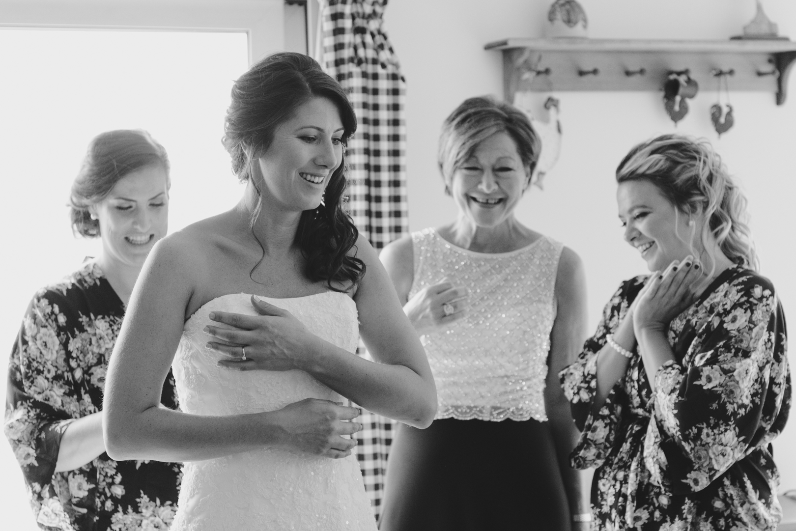 bridesmaids and mother of the bride helping bride into her dress