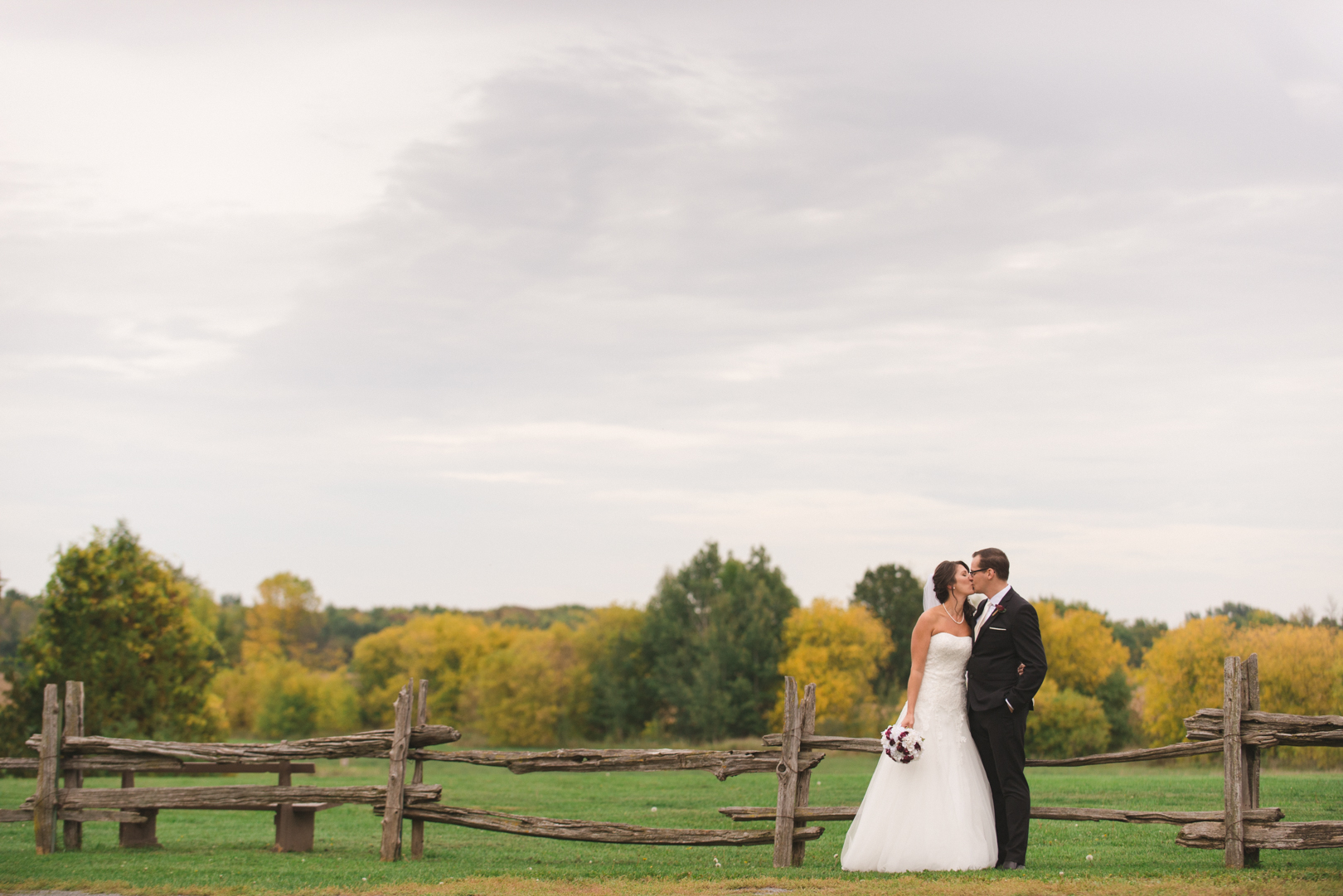 bride and groom kissing along old wooden fence in fields at strathmere in ottawa