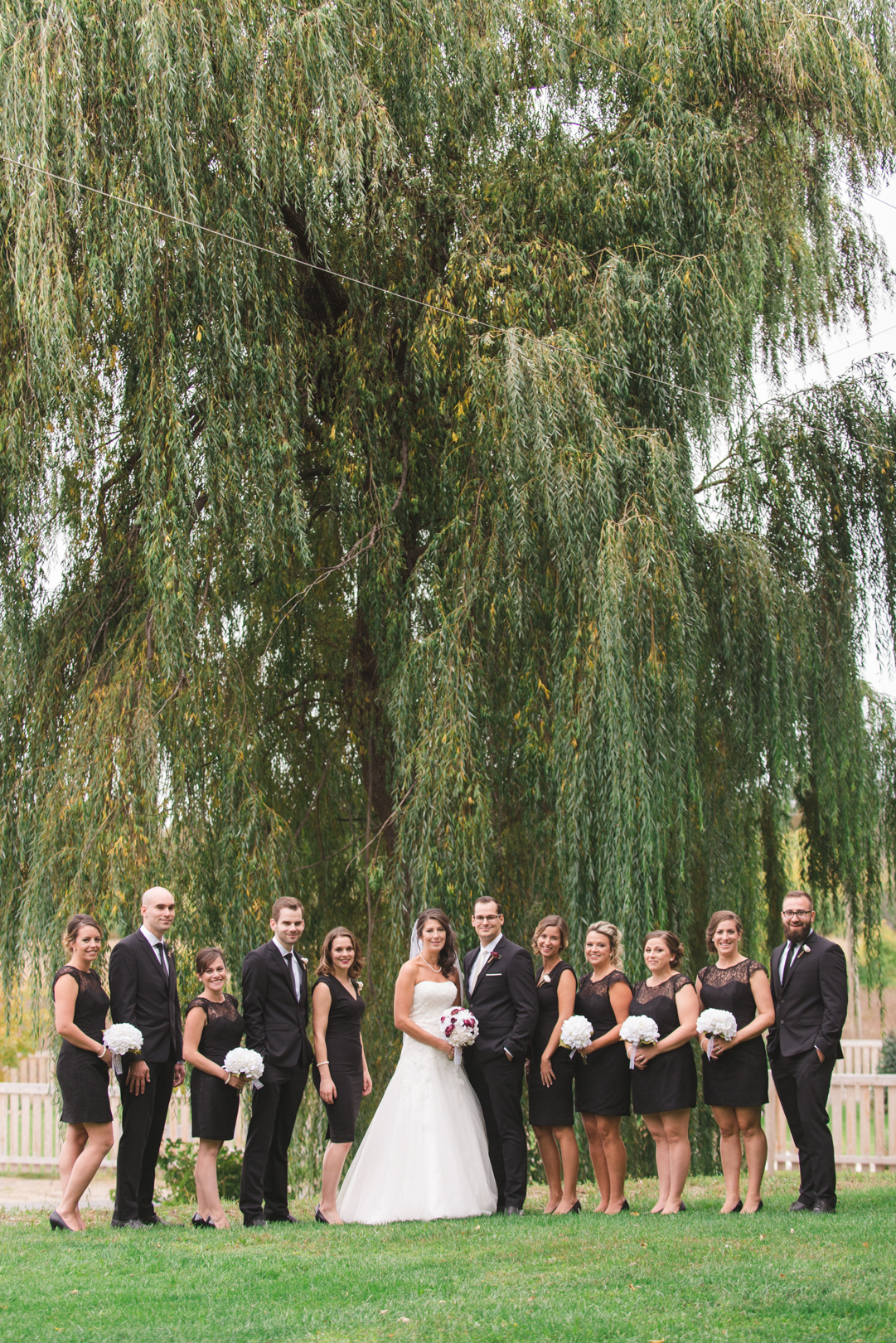 wedding party in all black standing in front of willow tree