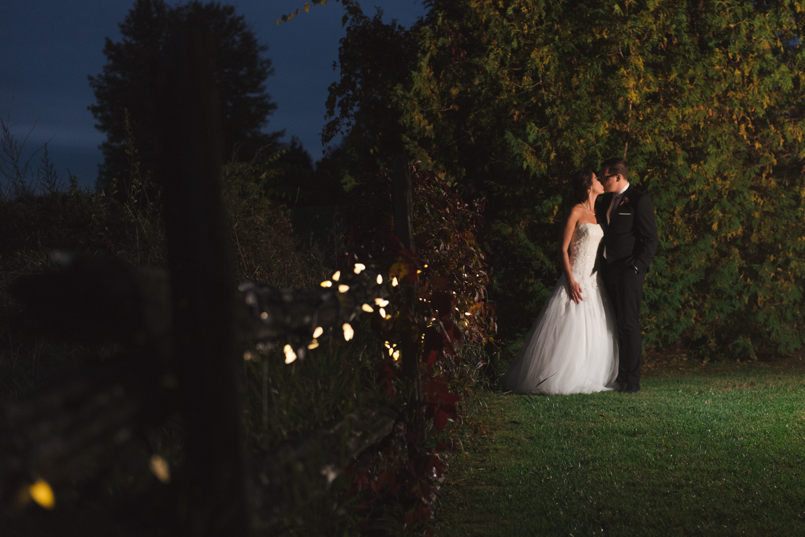 couple along a wooden fence with twinkly lights at night