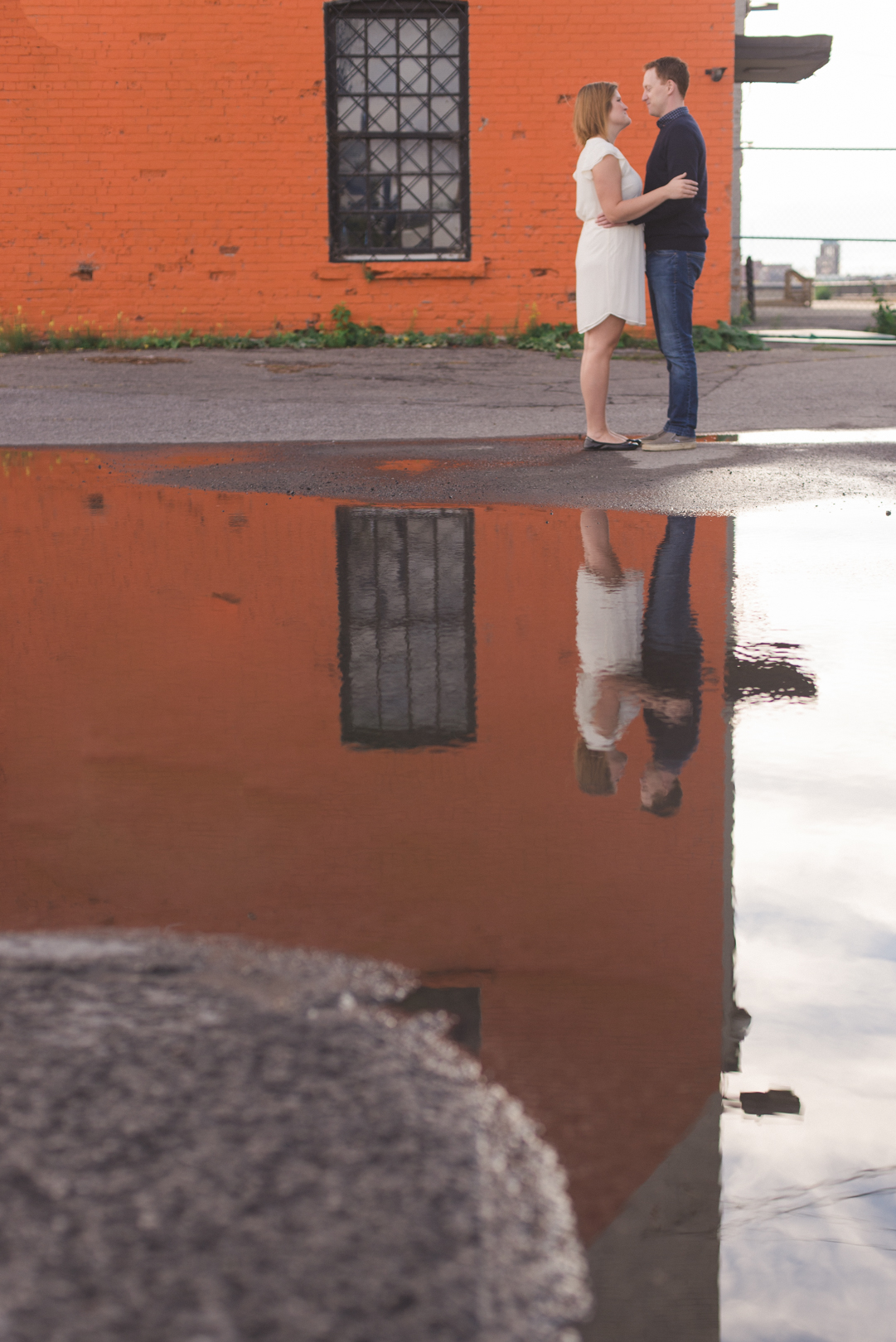 couple standing by orange brick building and reflection in puddle