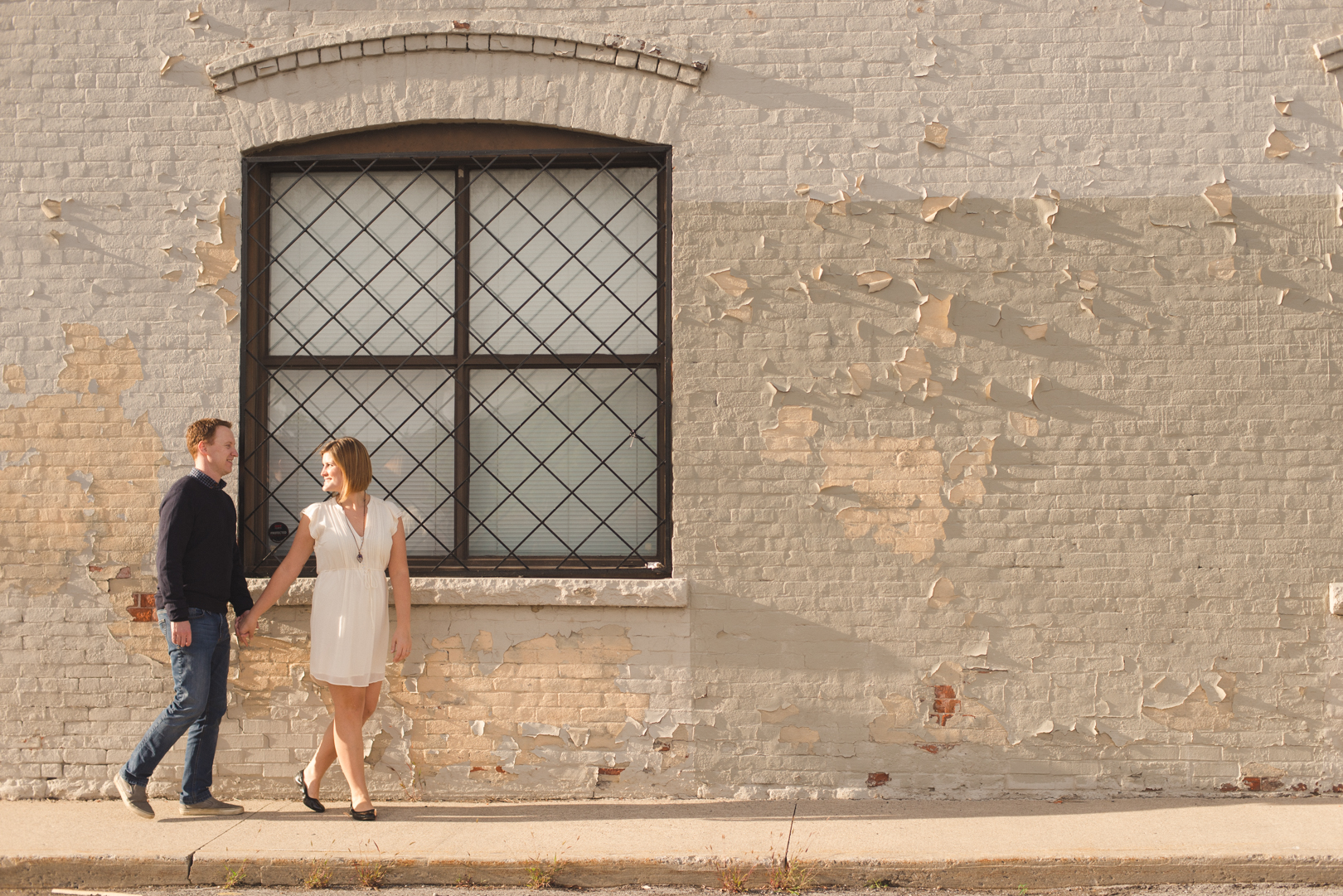 coupe walking along old brick building at sunset