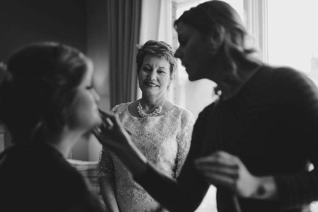 mother of the bride watching as her daughter gets her makeup done
