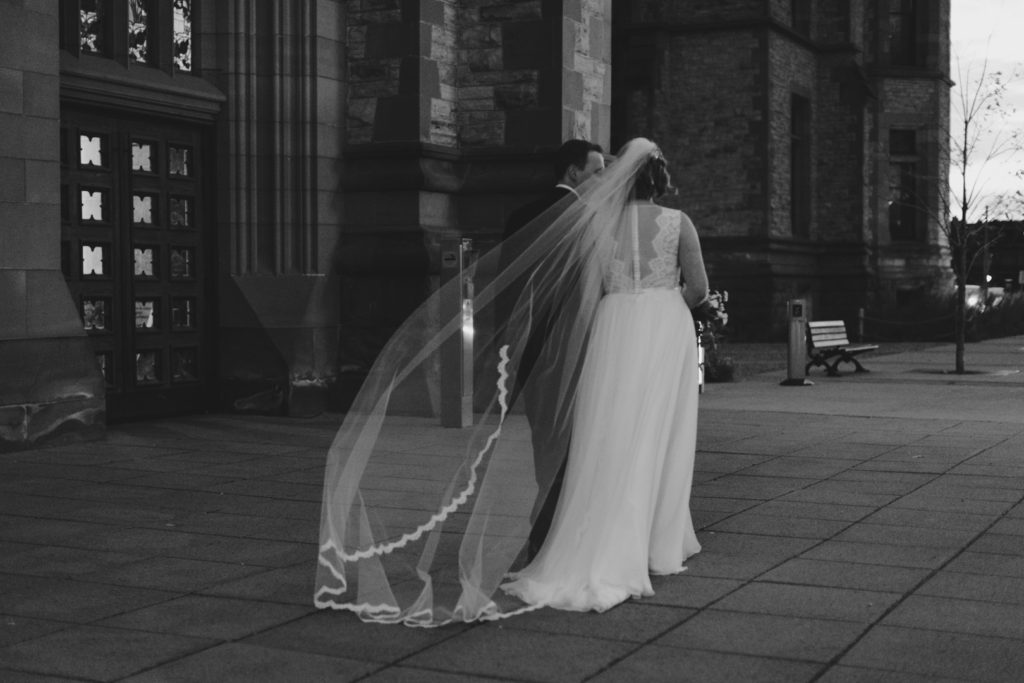 bride and groom walking as the bride's cathedral veil blows in the wind