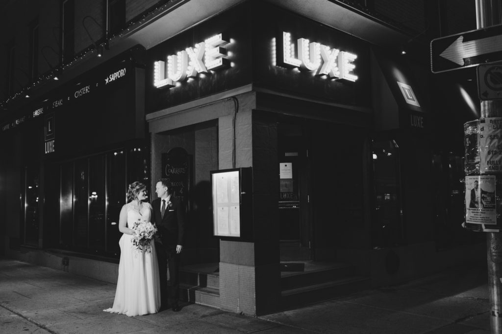 bride and groom standing outside of luxe bistro at night