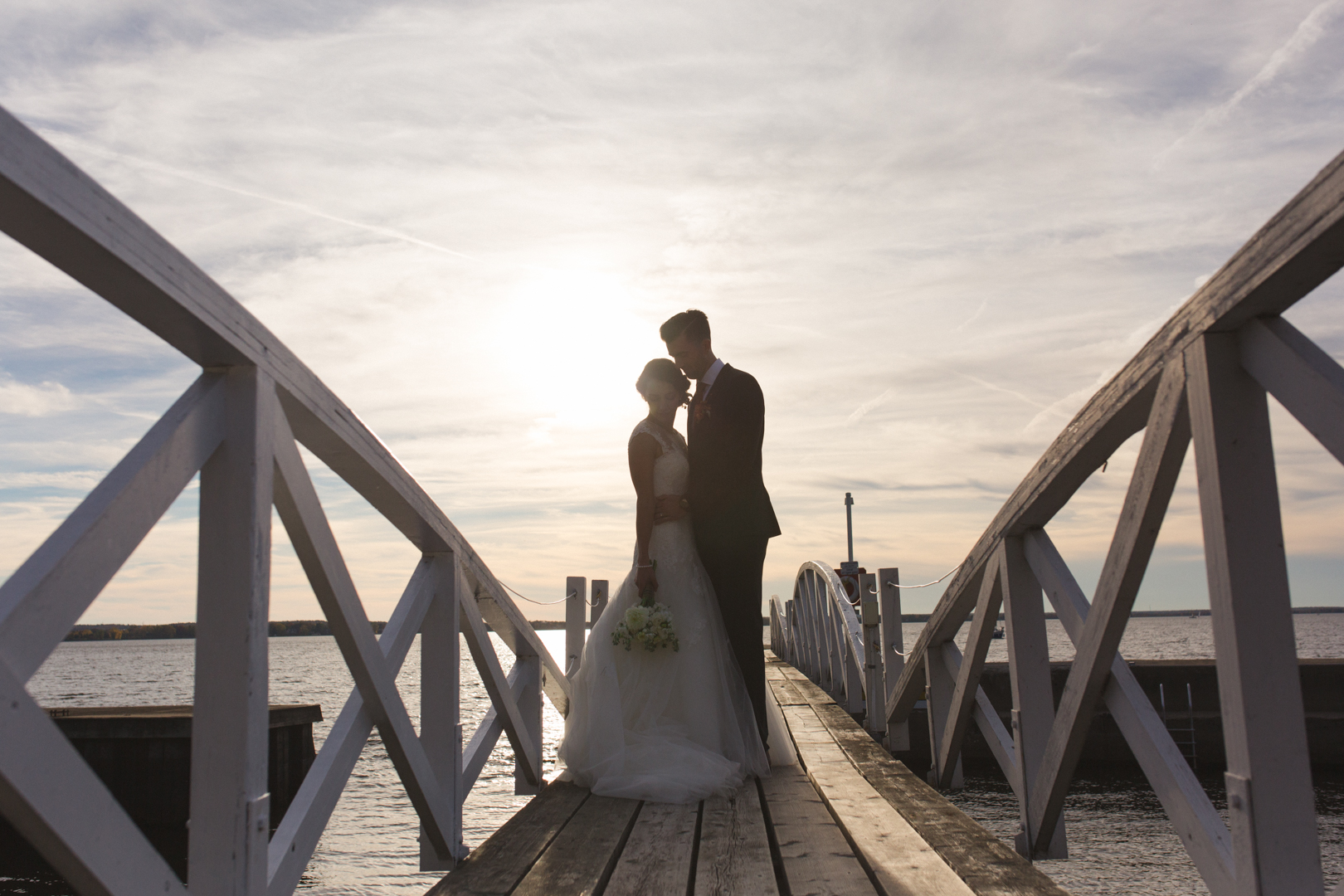 Silhouette of bride and groom standing together on little white bridge at sunset