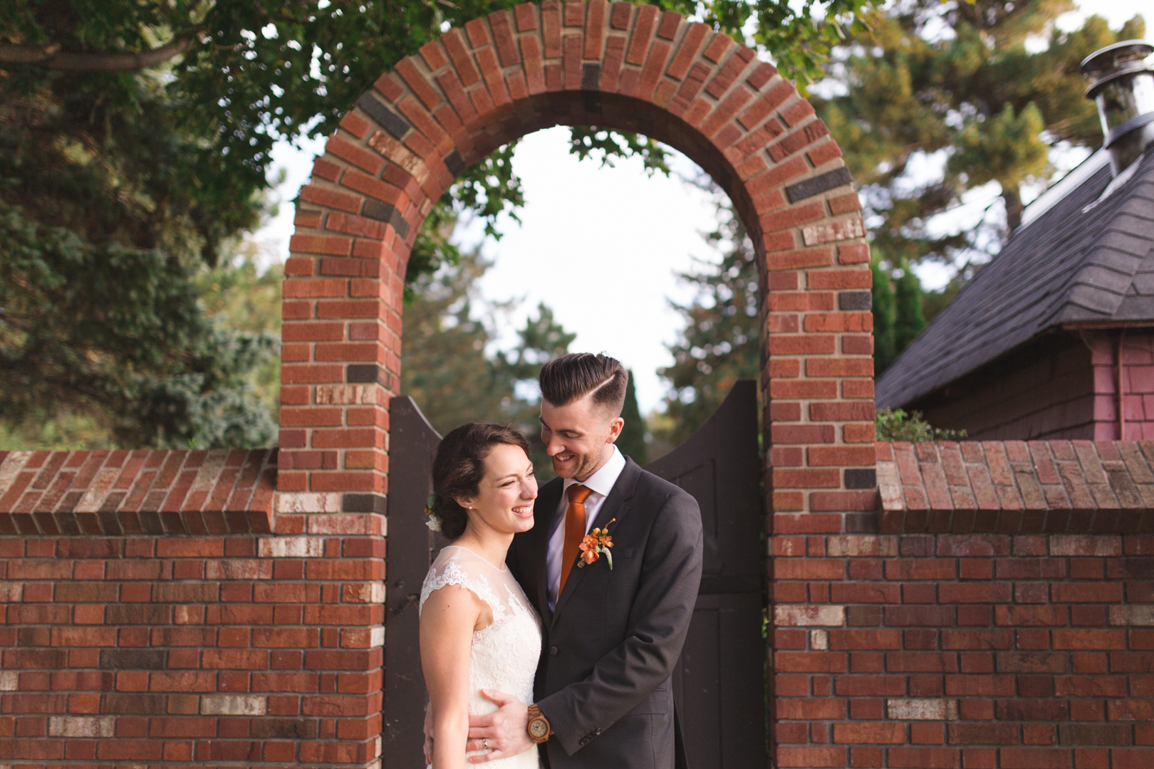 bride and groom laughing under brick archway