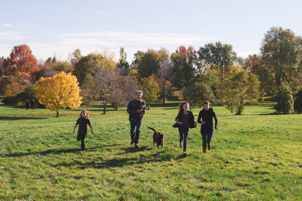 family running in the arboretum fields with their dog