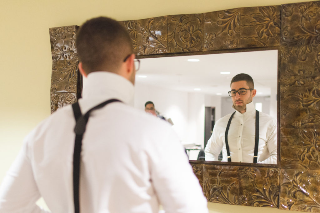 Groom adjusting his suspenders in the mirror