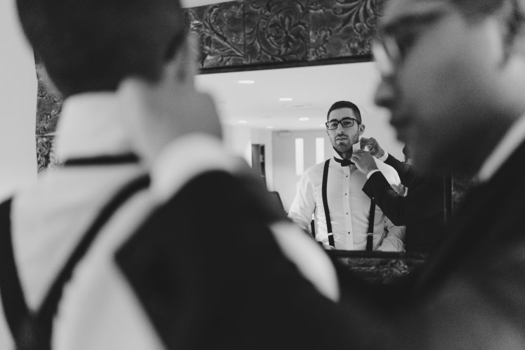 Groomsmen helping groom with his bowtie in the mirrow