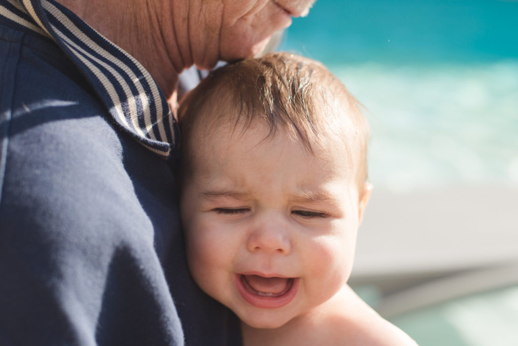 baby boy crying in grandpa's arm after swimming in cold pool