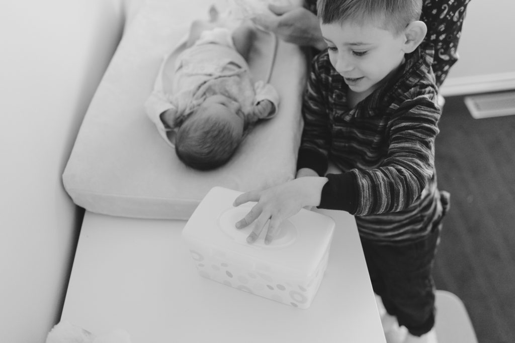big brother helping his mom change his baby sister's diaper