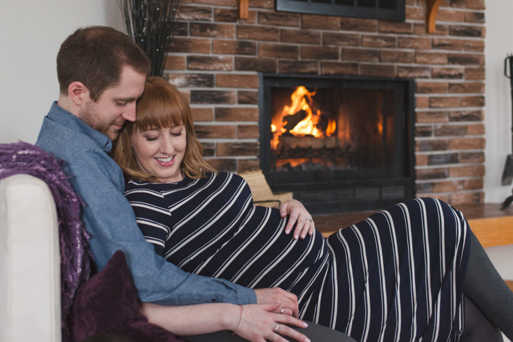 expecting couple cuddling at home on the couch by the fire