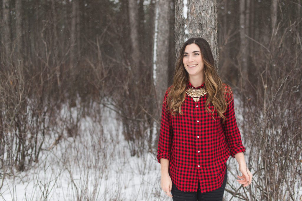 yoga teacher standing in a forest wearing bright red plaid shirt