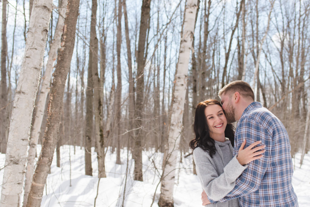 couple cuddling among the birch trees in winter