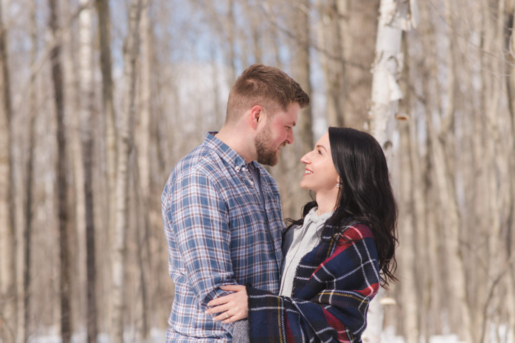 engaged couple cuddling among the birch trees in winter