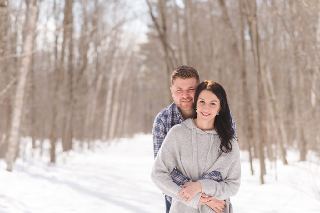 engaged couple cuddling on the snowy path in the sunlight in winter