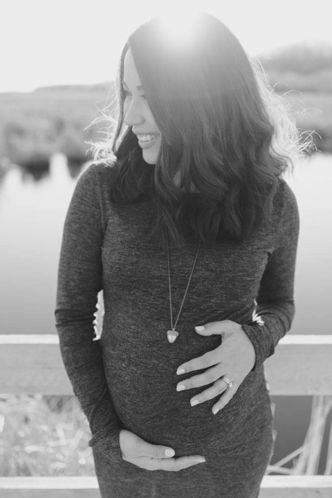 mother to be standing on wooden bridge at sunset in black and white