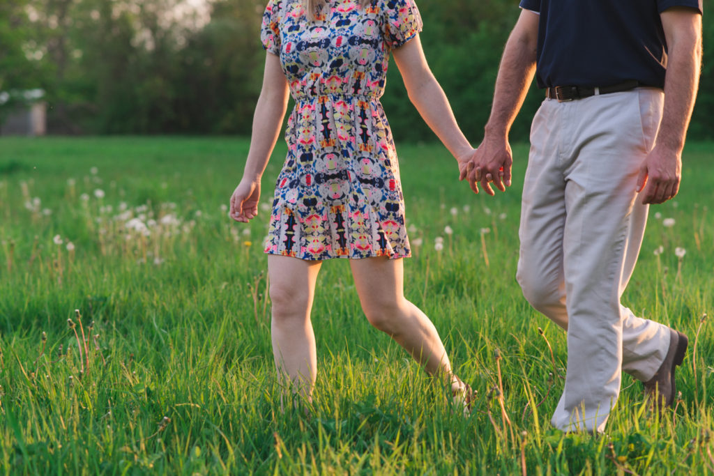 Couple holding hands walking in a field at sunset
