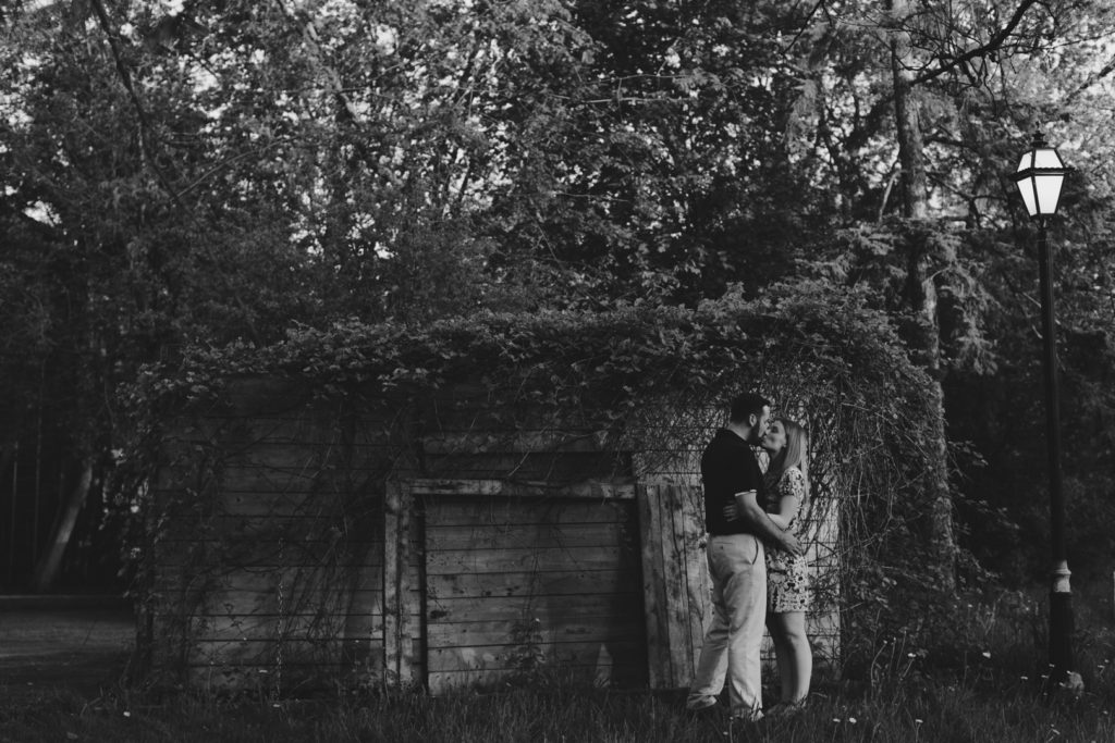 Couple standing in front of wooden shed at sunset in black and white