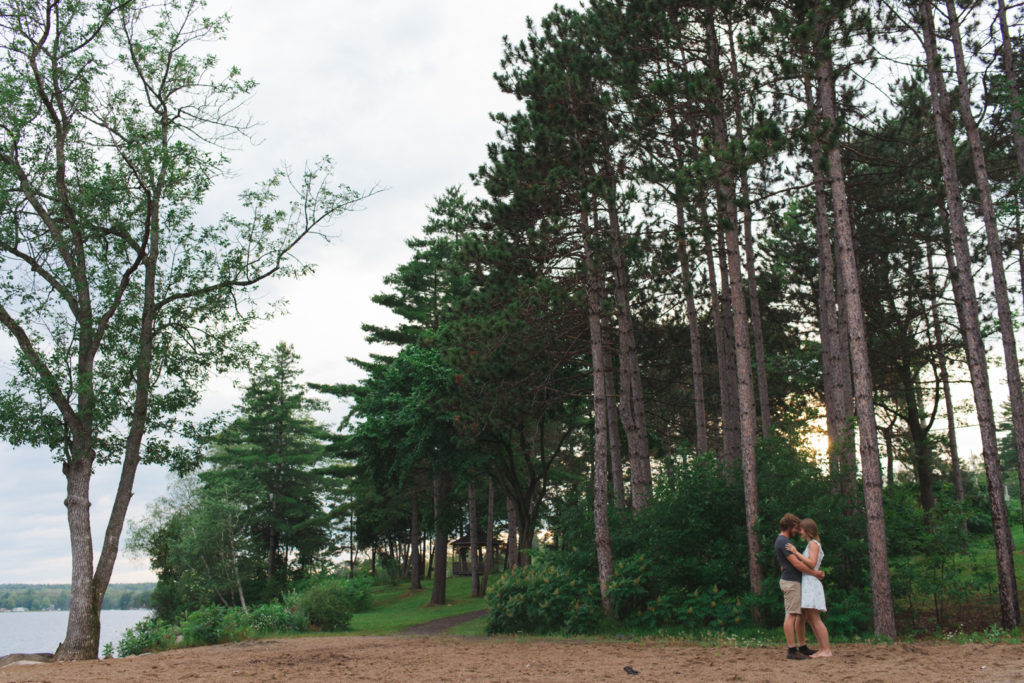 couple standing together with tall trees surrounding them at sunset