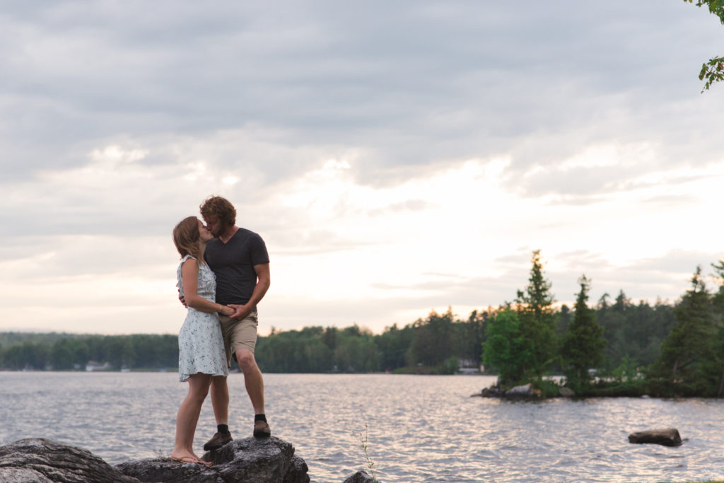 couple standing on rocks by the lake kissing
