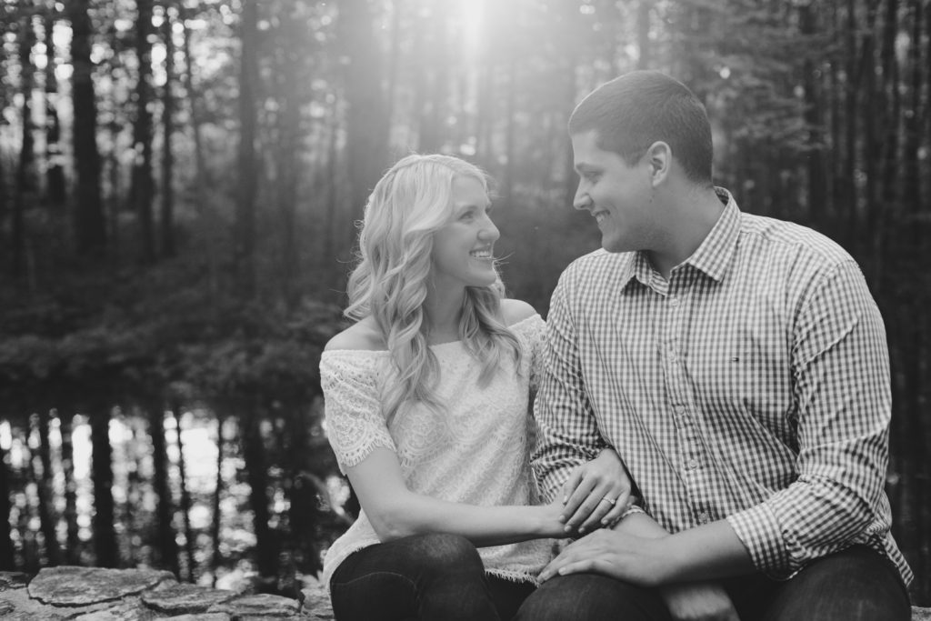 black and white photo of engaged couple sitting together among the trees at sunset