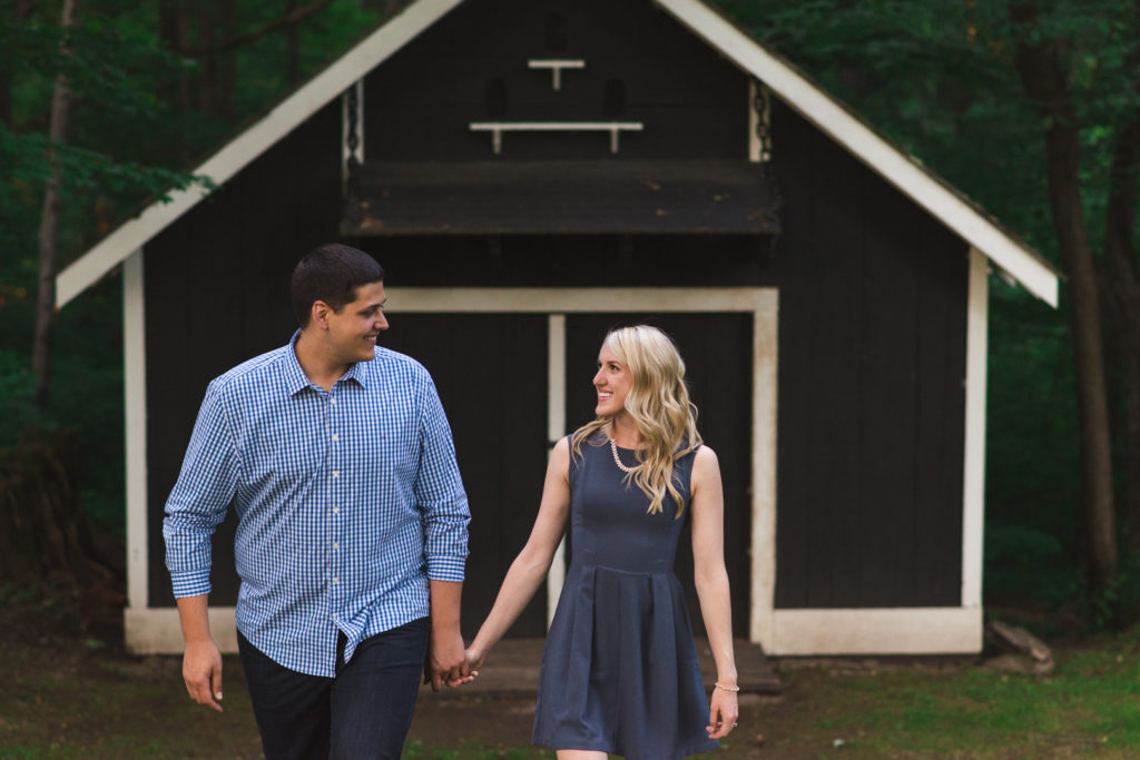 photo of engaged couple holding hands in front of black and white shed