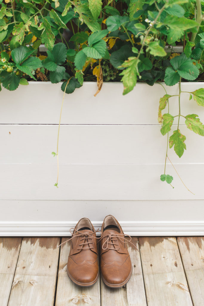 groom's brown wedding shoes in front of white and green planter