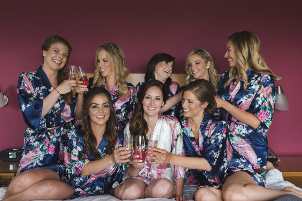 bride and bridesmaids in floral robes sitting on the bed together