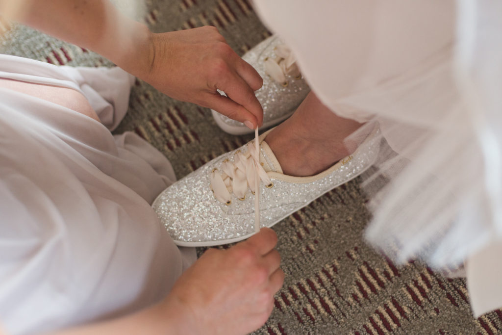 maid of honour tying up the bride's kate spade sparkly shoes