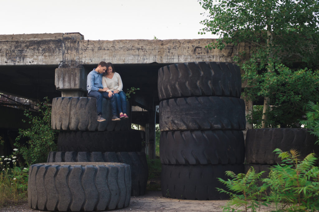engaged couple sitting on top of stacks of large black tires