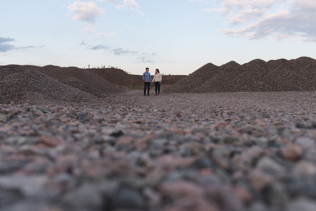 engaged coupe holding hands among quarry of gravel piles
