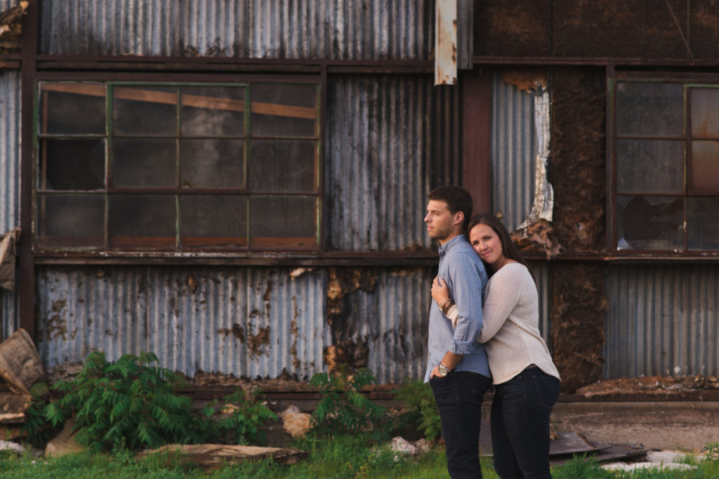 bride to be hugging her fiancee from behind outside abandoned building