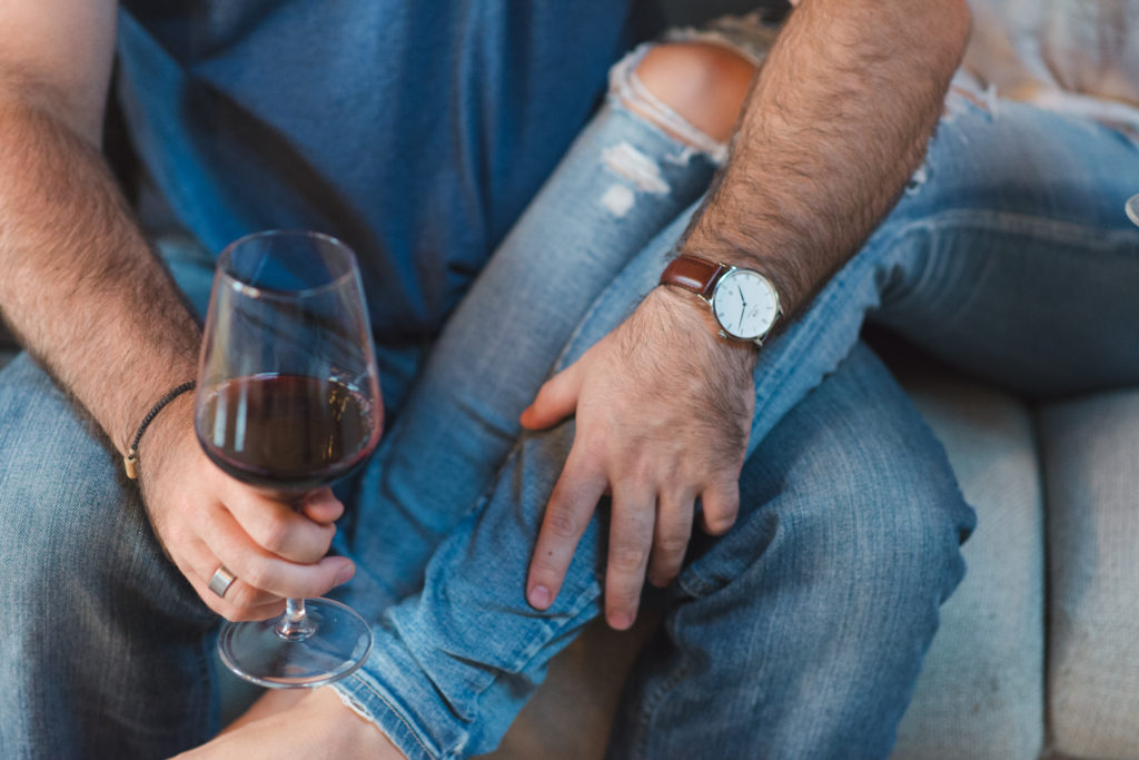 girl resting her legs in her man's lap while they drink wine on the couch