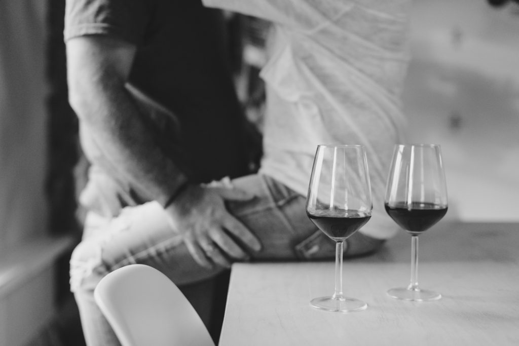 wine glasses resting on table while couple cuddle in the background